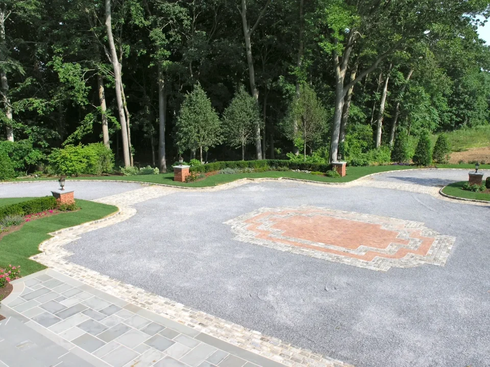 Elegant driveway with intricate brickwork design, surrounded by manicured greenery and trees.
