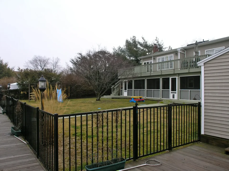 Backyard with a lawn, screened porch, deck, and a black fence