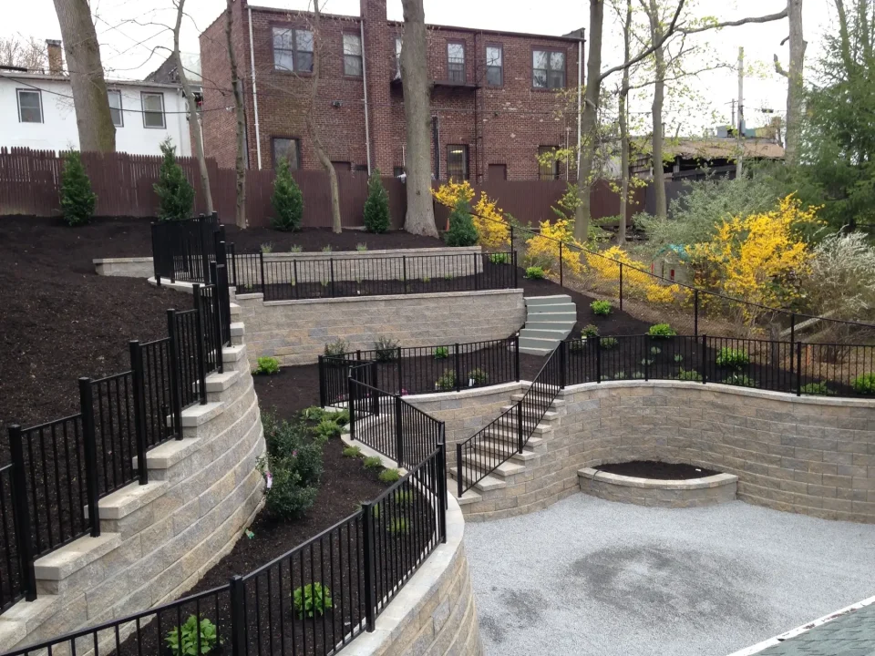 Tiered garden with stone walls, metal fences, staircases, and blooming shrubs.