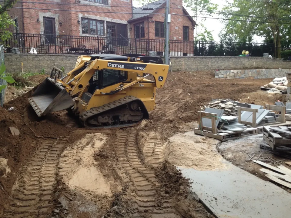 A yellow skid steer loader working on a construction site with dug-up earth and building materials.