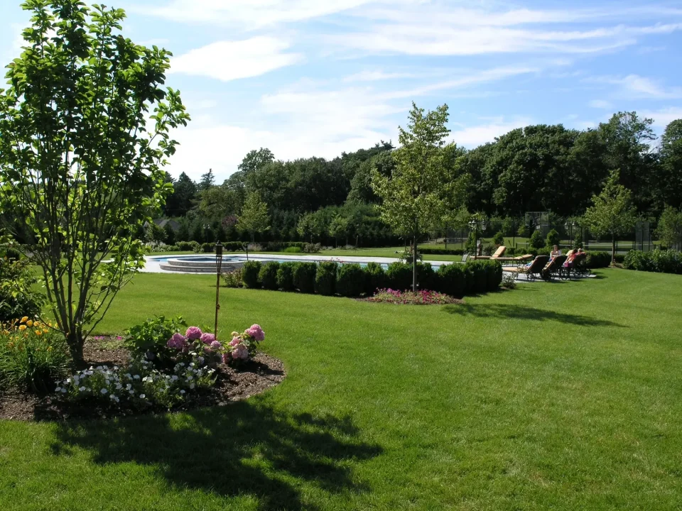 A well-manicured garden with trees, flowers, a lawn, and a small pond.
