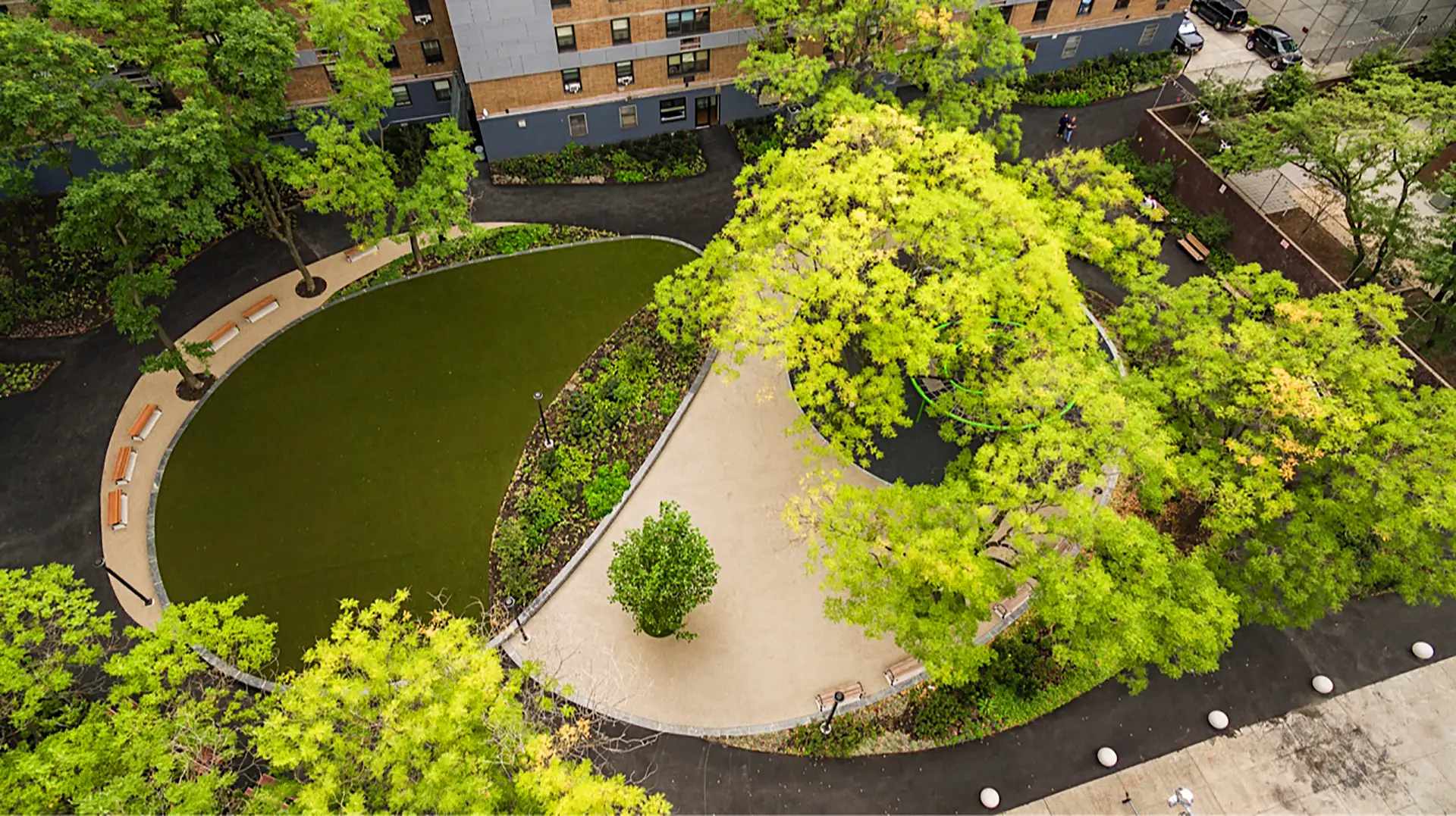 Aerial view of a park with a pond, walking path, benches, and lush green trees.