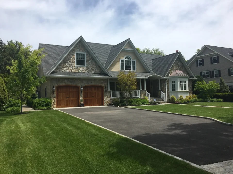 Large suburban home with stone facade, wooden garage doors, and manicured lawn.