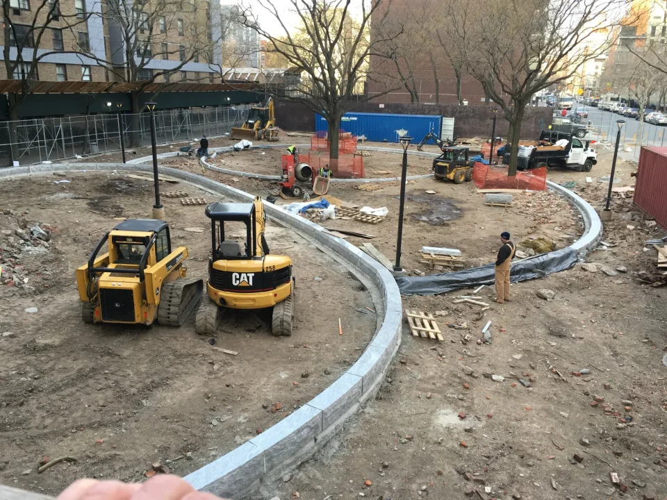Urban construction site with heavy machinery and a worker near a new curb.