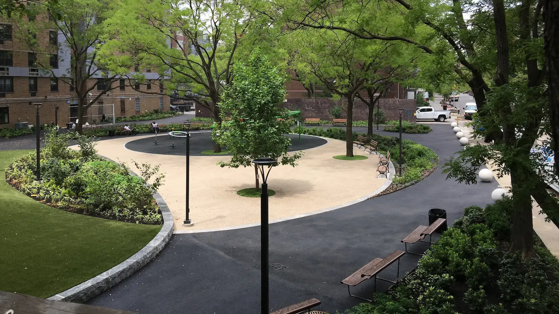 Urban park with curved paths, benches, lush greenery, and a playground.