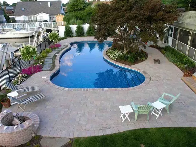 Aerial view of a kidney-shaped backyard pool with patio and lounging chairs.