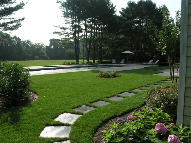 Lush garden with stepping stones leading to a pool, surrounded by trees and flowers.